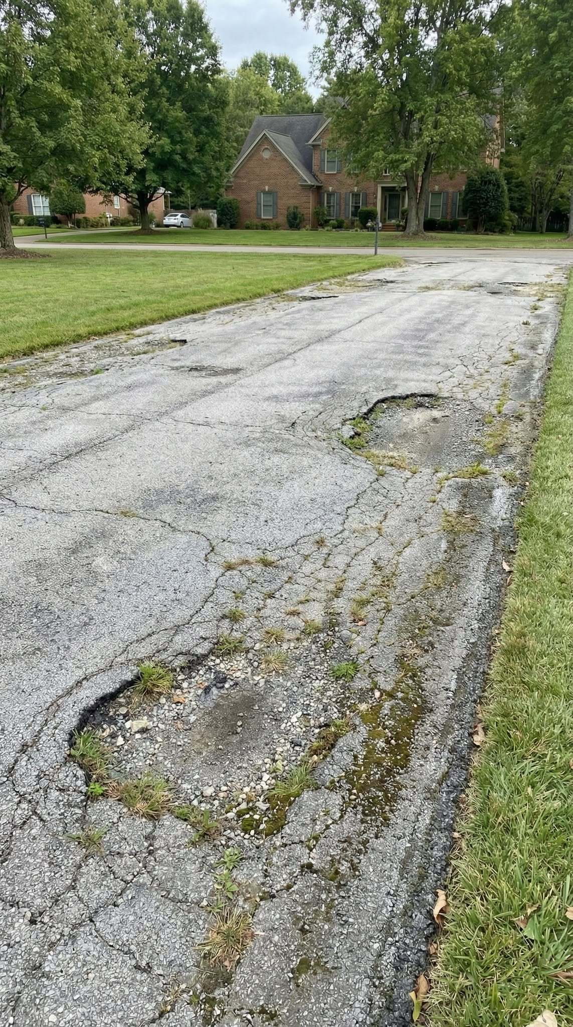 Driveway before — cracked, faded, and potholed asphalt